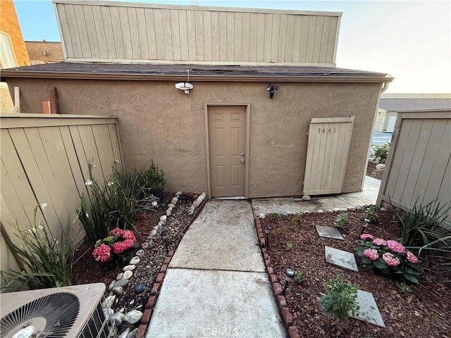 entrance to property with central AC unit, fence, and stucco siding