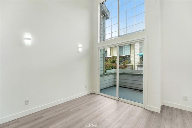 empty room with baseboards, wood finished floors, and a towering ceiling