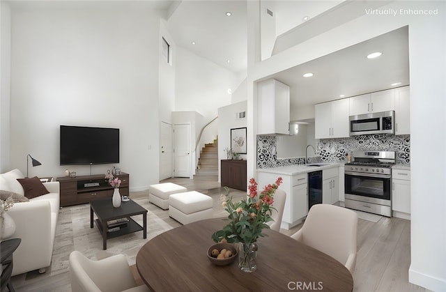 living area featuring stairs, baseboards, high vaulted ceiling, recessed lighting, and light wood finished floors