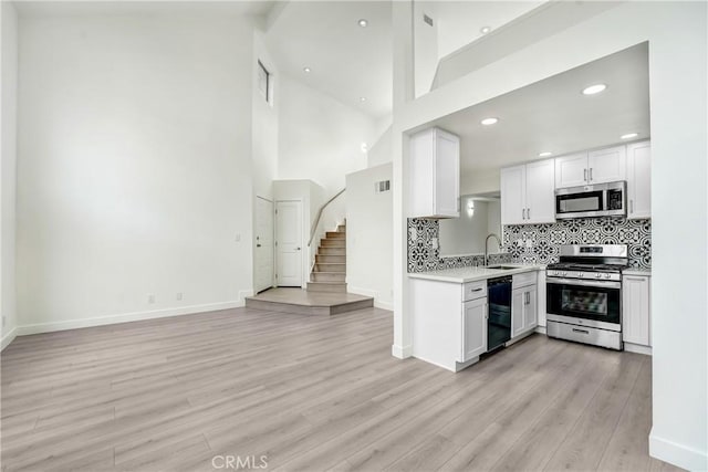 kitchen featuring appliances with stainless steel finishes, a sink, light wood-style floors, light countertops, and decorative backsplash