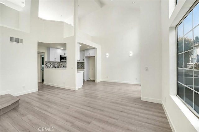 unfurnished living room featuring visible vents, light wood finished floors, and baseboards