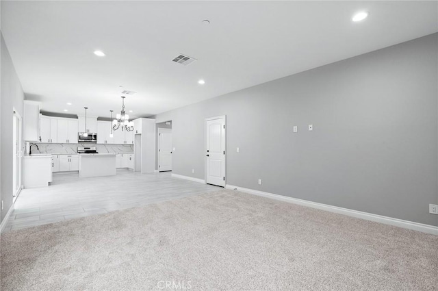 unfurnished living room with visible vents, recessed lighting, a notable chandelier, and light carpet
