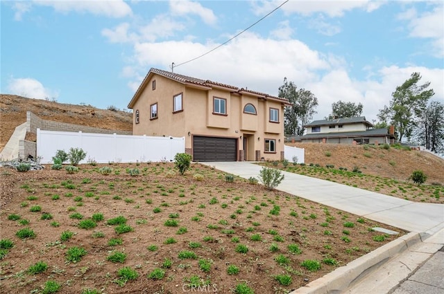 view of front facade featuring an attached garage, driveway, stucco siding, and fence