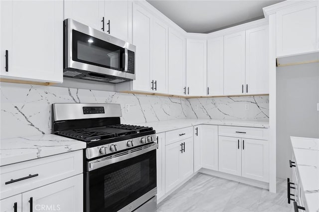 kitchen with white cabinetry, appliances with stainless steel finishes, marble finish floor, light stone counters, and decorative backsplash
