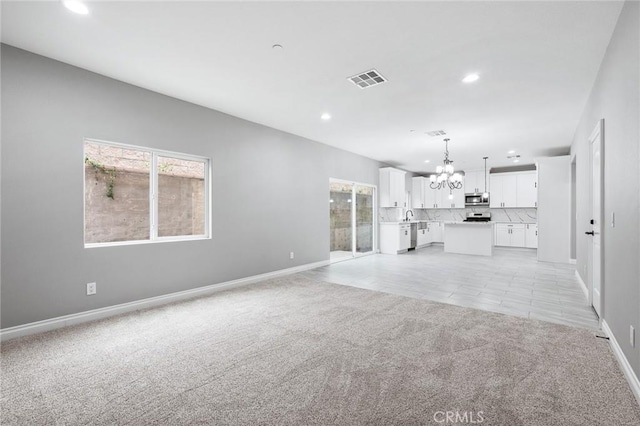 unfurnished living room with baseboards, an inviting chandelier, light carpet, recessed lighting, and visible vents