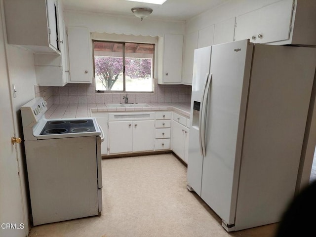 kitchen featuring white appliances, white cabinets, a sink, decorative backsplash, and tile counters