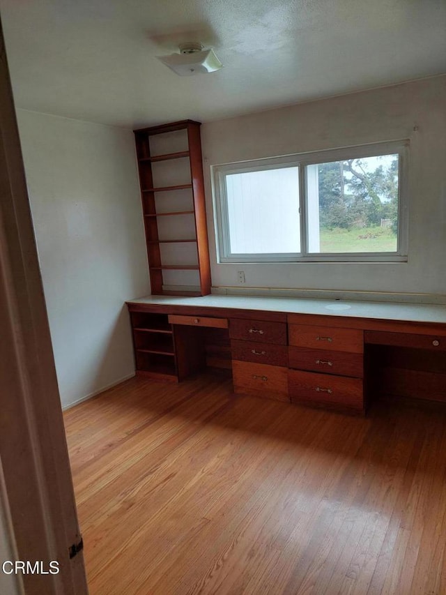 unfurnished office with built in desk, light wood-style floors, and a healthy amount of sunlight