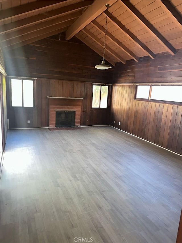 unfurnished living room with wood finished floors, wooden walls, vaulted ceiling with beams, and a brick fireplace
