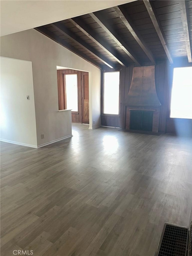 additional living space with baseboards, wood finished floors, lofted ceiling with beams, and a fireplace