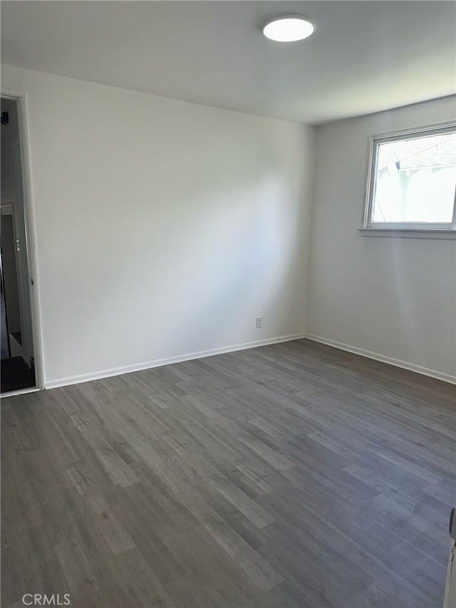 unfurnished room with baseboards and dark wood finished floors