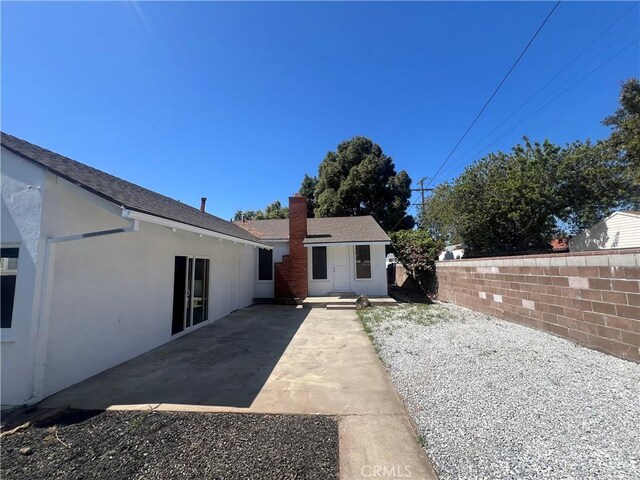 rear view of house featuring a chimney, a patio area, stucco siding, and fence