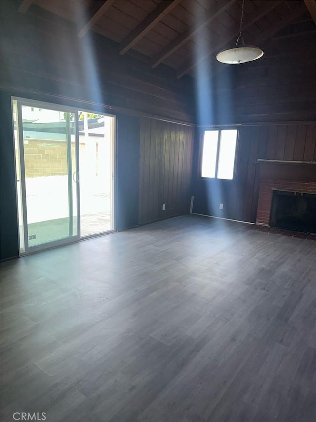 unfurnished living room featuring wood walls, vaulted ceiling with beams, wood finished floors, and a brick fireplace