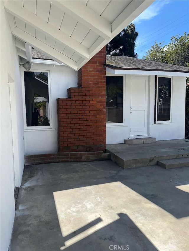 property entrance with a patio, stucco siding, and brick siding