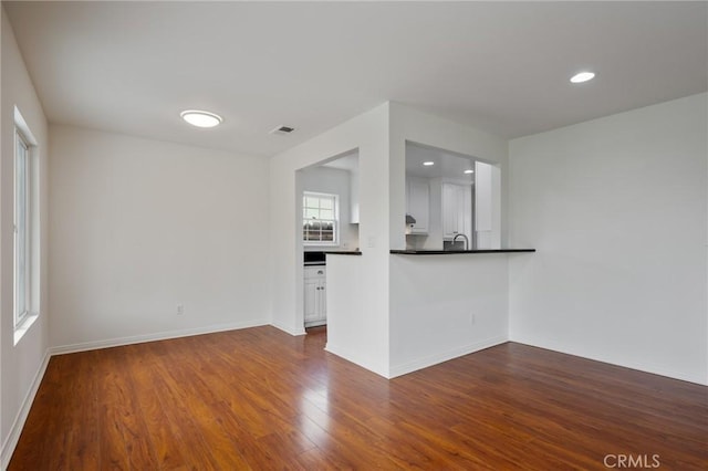 unfurnished living room featuring baseboards, recessed lighting, dark wood-type flooring, visible vents, and a sink