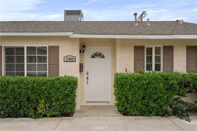 property entrance featuring a shingled roof and stucco siding