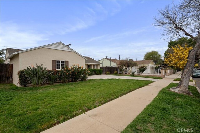 view of side of home with driveway, stucco siding, fence, and a lawn