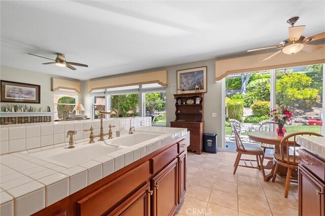 kitchen with tile countertops, a ceiling fan, a sink, and light tile patterned floors