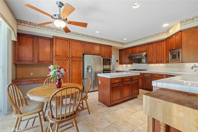 kitchen with stainless steel appliances, a sink, under cabinet range hood, light tile patterned floors, and ceiling fan
