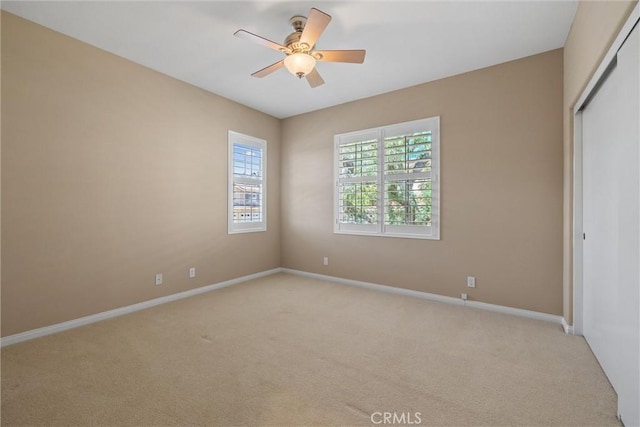 unfurnished bedroom featuring light colored carpet, a closet, baseboards, and ceiling fan