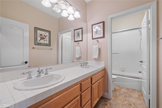 full bath with double vanity, toilet, and bath / shower combo with glass door