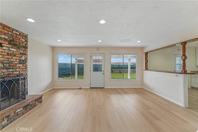1114 Stovall Ave, La Puente, CA 91745 - unfurnished living room with a brick fireplace, light wood-style flooring, a textured ceiling, and a healthy amount of sunlight