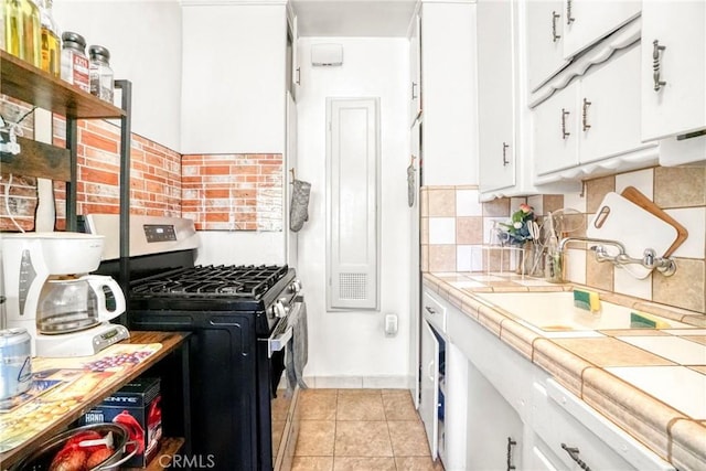 kitchen with white cabinetry, gas range, decorative backsplash, tile countertops, and a sink