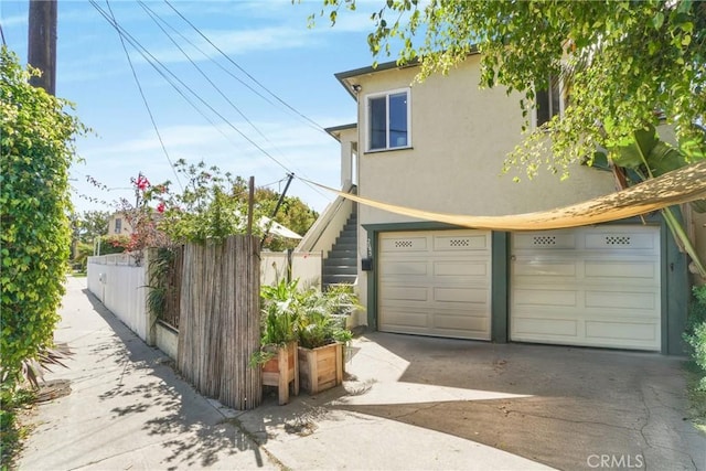 view of side of property with driveway, stucco siding, fence, and an attached garage