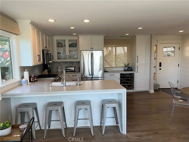 kitchen with appliances with stainless steel finishes, wine cooler, a sink, a peninsula, and glass insert cabinets