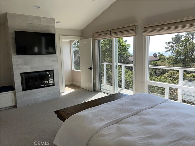 bedroom featuring a tiled fireplace, lofted ceiling, multiple windows, and access to exterior