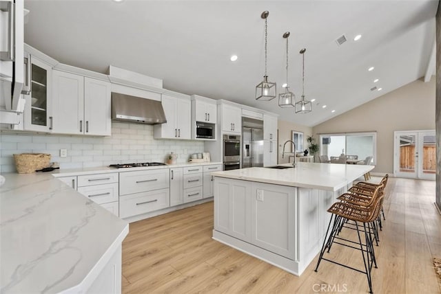 625 Calle Miguel, San Clemente, CA 92672 - kitchen featuring appliances with stainless steel finishes, decorative backsplash, light wood finished floors, white cabinets, and wall chimney range hood