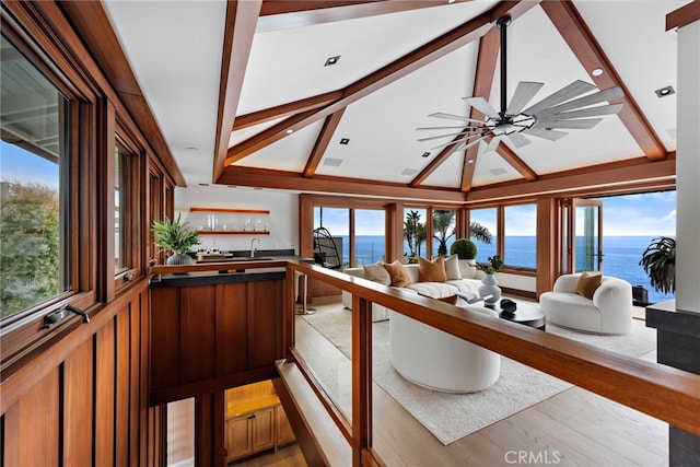 living area with a water view, lofted ceiling with beams, a ceiling fan, and wet bar