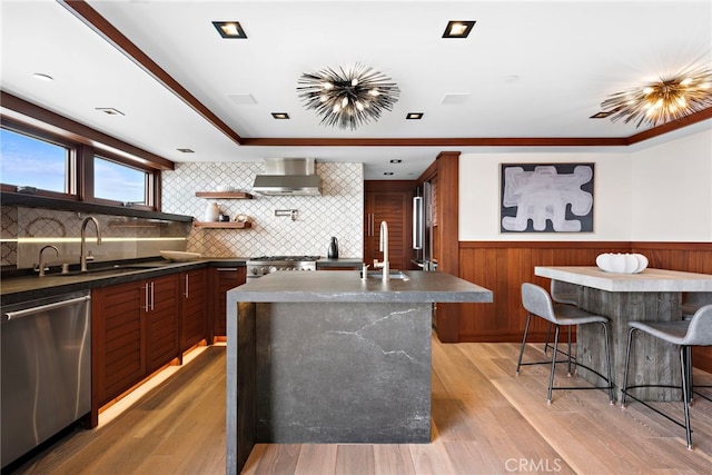 kitchen with wall chimney range hood, dark countertops, wainscoting, a sink, and stainless steel appliances