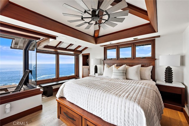 bedroom with a water view, multiple windows, light wood finished floors, and a raised ceiling