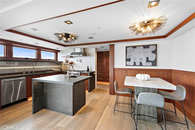 kitchen with wall chimney range hood, a sink, a raised ceiling, dishwasher, and a kitchen island with sink