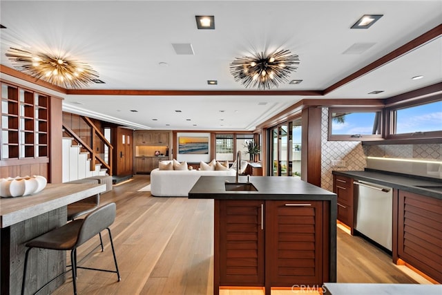 kitchen featuring dark countertops, a sink, light wood finished floors, a center island, and stainless steel dishwasher