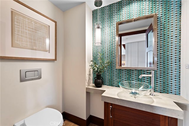 half bath with toilet, baseboards, and vanity