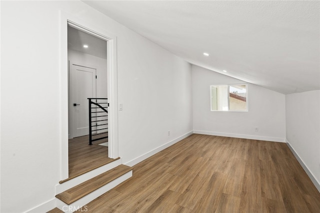 additional living space with baseboards, vaulted ceiling, wood finished floors, and recessed lighting