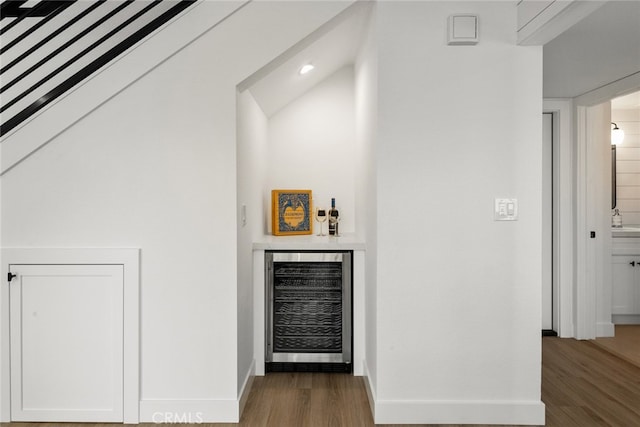 bar featuring beverage cooler, a bar, baseboards, and wood finished floors