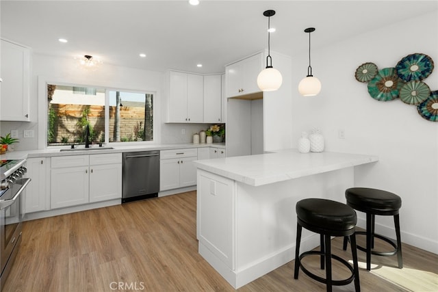 kitchen with a sink, a breakfast bar, light wood-style flooring, a peninsula, and appliances with stainless steel finishes