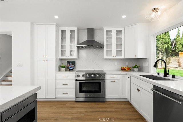 kitchen with backsplash, wall chimney range hood, stainless steel appliances, and a sink