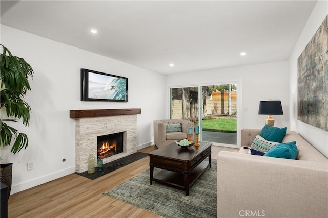 living area with baseboards, a stone fireplace, wood finished floors, and recessed lighting