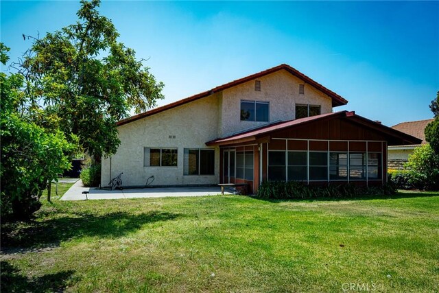 back of house featuring a patio area, a sunroom, a yard, and stucco siding