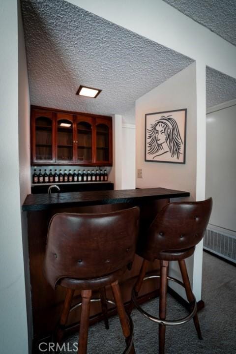 bar with visible vents, a dry bar, carpet flooring, and a textured ceiling