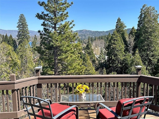 deck with outdoor dining area, a mountain view, and a forest view