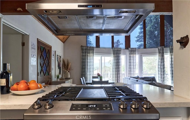 kitchen with wall chimney range hood, stovetop, open floor plan, and a wealth of natural light