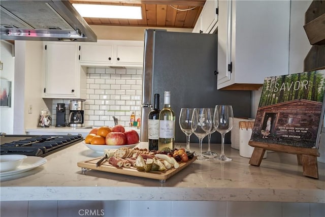 kitchen featuring freestanding refrigerator, gas cooktop, ventilation hood, white cabinetry, and backsplash