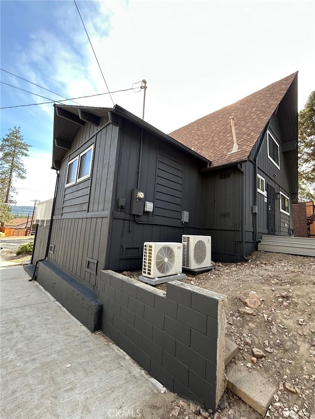 view of property exterior with a shingled roof, board and batten siding, and ac unit