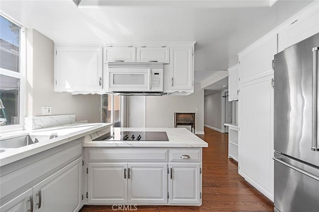 kitchen featuring dark wood finished floors, freestanding refrigerator, white microwave, black electric stovetop, and white cabinetry