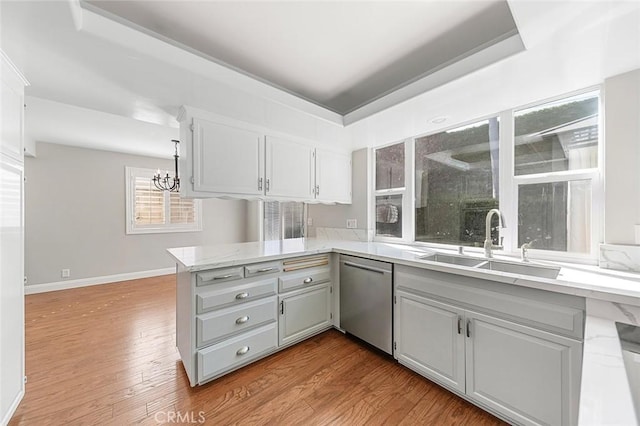 kitchen with a peninsula, wood finished floors, a chandelier, a sink, and dishwasher