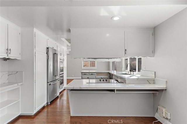 kitchen featuring appliances with stainless steel finishes, a sink, light stone counters, a peninsula, and white cabinetry
